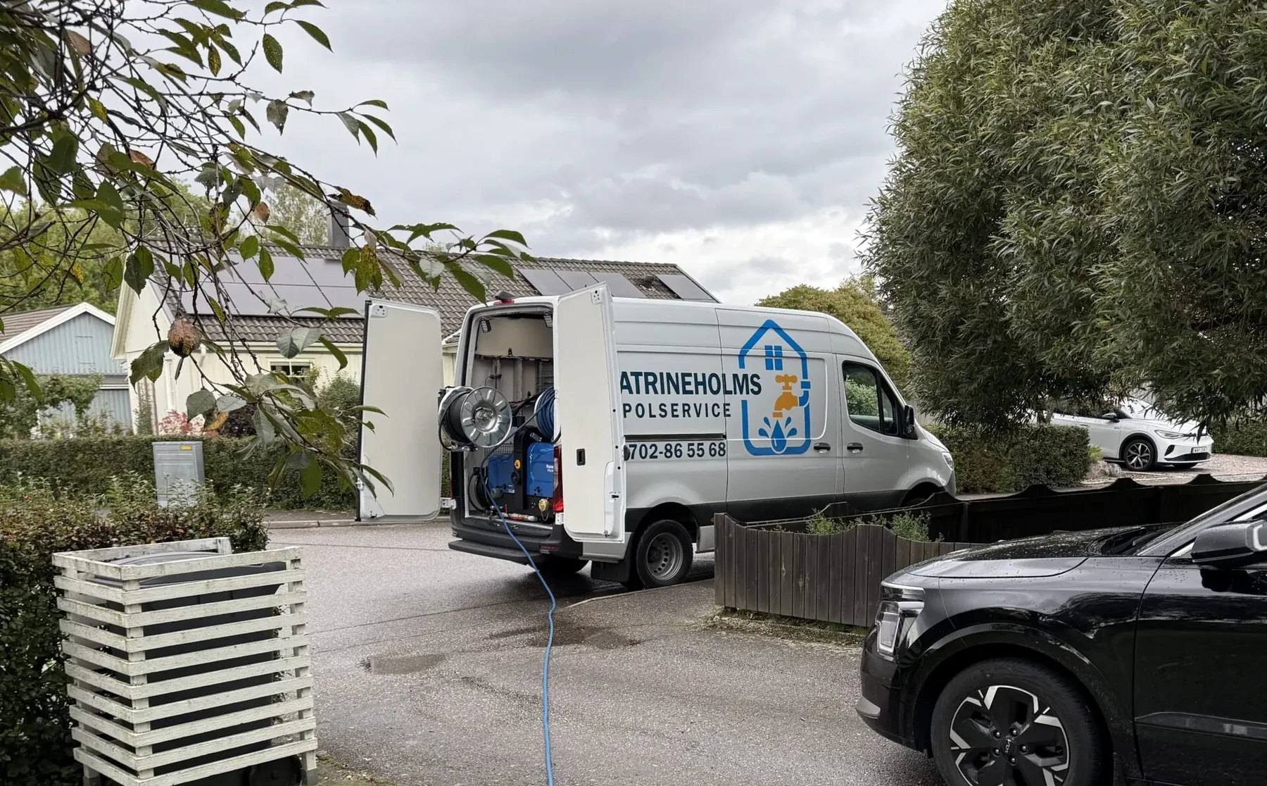 Servicebilen med spolslang över gräsmattan vid en villa