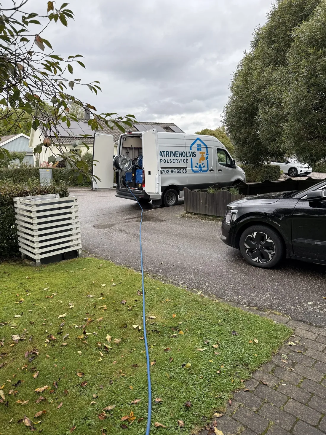 Servicebilen med spolslang över gräsmattan vid en villa